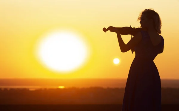 Silhouette einer weiblichen Figur, die bei Sonnenuntergang den Vioylin spielt, Frau entspannt sich in klassischer Musik, Performance über die Natur, Konzept-Klangkunst — Stockfoto