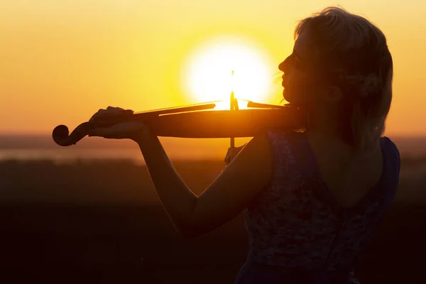 Silueta del perfil facial de una figura femenina tocando el violín al atardecer, actuación sobre la naturaleza, chica con instrumento musical bajo la barbilla, concepto de arte musical — Foto de Stock