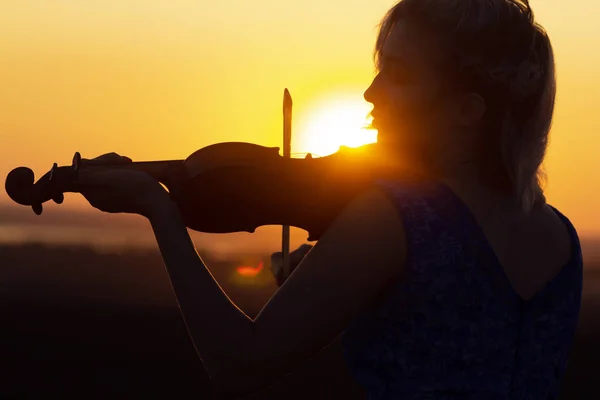 Silueta del perfil facial de una figura femenina tocando el violín al atardecer, actuación sobre la naturaleza, chica con instrumento musical bajo la barbilla, concepto de arte musical — Foto de Stock