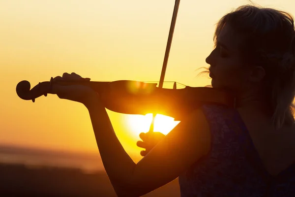 Silueta de chica llevando el arco a lo largo de las cuerdas tocando el violín al atardecer, actuación en la naturaleza, concepto de arte musical e inspiración — Foto de Stock