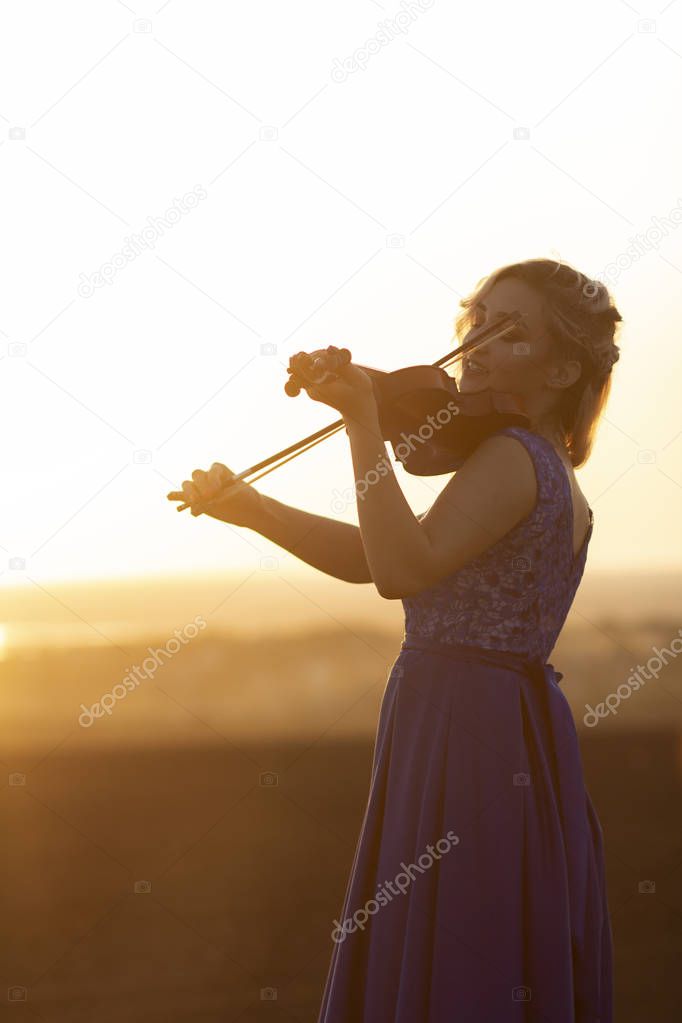 silhouette of a female figure playing the vio and hobbylin at sunset, woman relaxing in music, performance on nature, concept art