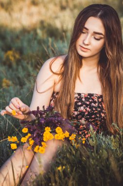 Çayırda bir buket kır çiçeğiyle güzel bir kız, uzun saçlı, doğada yürüyen genç bir kadın, köyde yazın çekilen narin bir fotoğraf.
