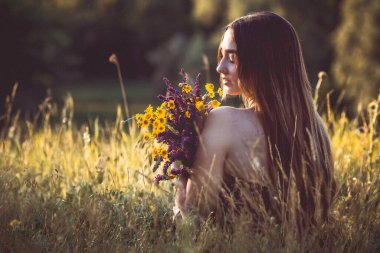Çayırda bir buket kır çiçeğiyle güzel bir kız, uzun saçlı, doğada yürüyen genç bir kadın, köyde yazın çekilen narin bir fotoğraf.