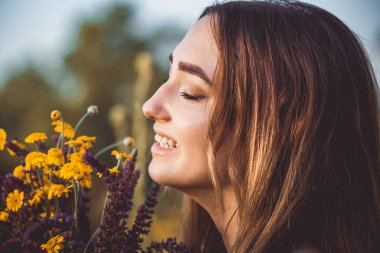 Çayırda bir buket kır çiçeğiyle güzel bir kız, uzun saçlı, doğada yürüyen genç bir kadın, köyde yazın çekilen narin bir fotoğraf.