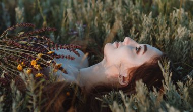 Bir buket kır çiçeğiyle çimenlerin üzerinde uzanan güzel kızın yakın plan yüzü, doğada uzun saçlı genç bir kadın, köyde yazın çekilen narin bir fotoğraf.
