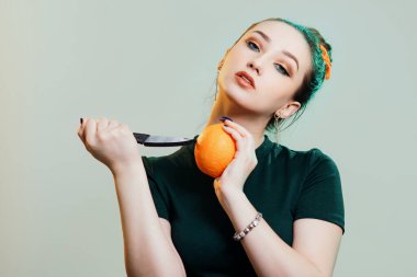 Portakal meyvesine bıçak dayamış güzel bir genç kadının portresi. Eller, stüdyo arkasında moda portresi yeşil ışıkla