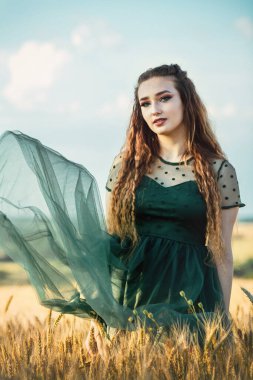 Yeşil etekli güzel bir kadın, gün batımında buğday kulaklarıyla tarlada yürüyen bir kız, yaz doğasının tadını çıkaran bir kız, özgürlük.