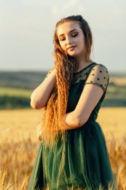 Yeşil elbiseli romantik bir kadın buğday tarlasında yürüyor uzun saçlı bir kız yaz doğasının, yaşam tarzının tadını çıkarıyor.