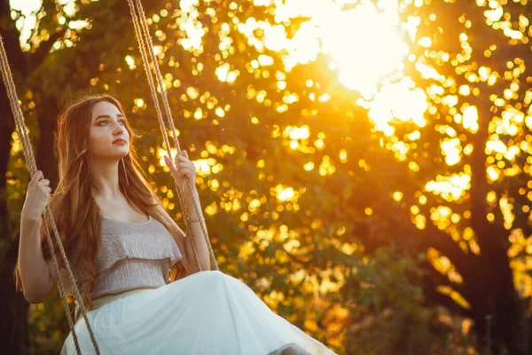 夏の大自然の中でロープスイングで長い髪のスイングを持つ美しい女の子Arの夕日 若い女性は木の枝の間で飛行を楽しむ レジャー活動 ライフスタイルコンセプト — ストック写真