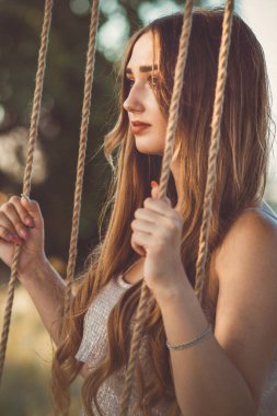 Uzun saçlı güzel bir kız salıncakta sallanıyor yaz doğasında, gün batımında dinlenen genç bir kadın boş zaman aktivitesi, yaşam tarzı konsepti.