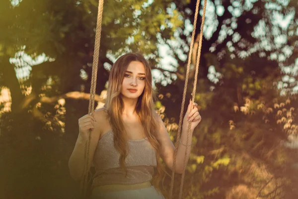 美丽的女孩 长发缠绕着绳子 在夏日的自然中荡秋千 年轻女子在日落时放松 休闲活动 生活方式的概念 — 图库照片