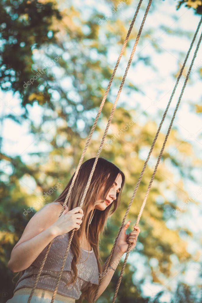 beautiful girl with long hair swinging on rope swing on summer nature, young woman relaxing at sunset, leisure activity, lifestyle concept