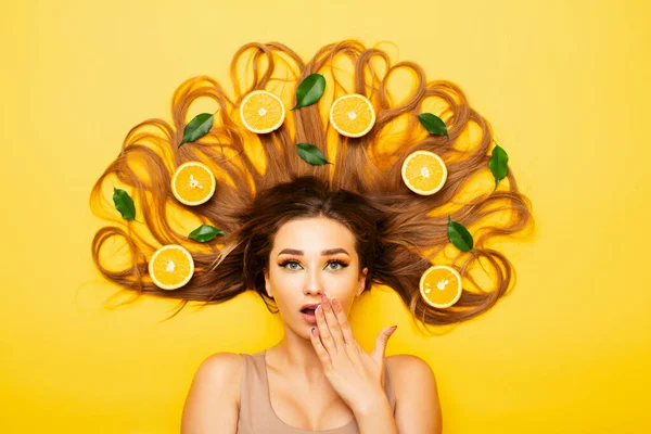Удивленная Девушка Лежит Ярком Студийном Фоне Апельсиновыми Фруктами Длинных Волосах — стоковое фото