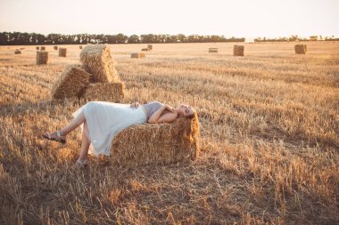 Genç bir kadın yaz akşamı samanlıkta yürürken, gün batımında açık havada uzun saçlı güzel romantik bir kız.