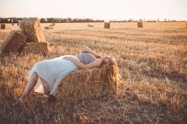 Genç bir kadın yaz akşamı samanlıkta yürürken, gün batımında açık havada uzun saçlı güzel romantik bir kız.