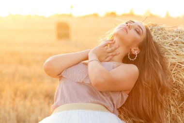 Genç bir kadın yaz akşamı samanlıkta yürürken, gün batımında açık havada uzun saçlı güzel romantik bir kız.
