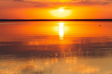 Deniz ufkunda gün batımının arka planı, su boşluğunda bulutların yansıması bulanıklaşır.