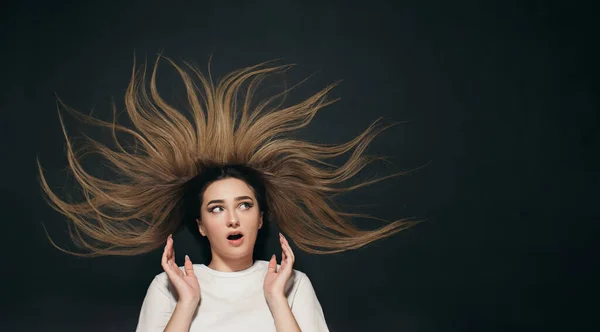 portrait of young surprised woman with long hair lying on black studio background, female face expression of shock and delight top view
