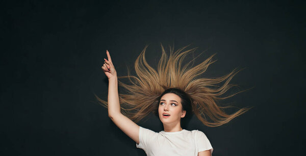 young delighted woman lying on black studio background and pointing up by pencil top view,advertising concept with place for text