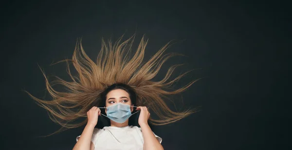 young woman removes the mask from the face on black studio background top view, concept quarantine