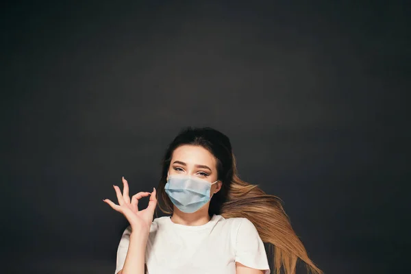 스튜디오 백그라운드 뷰에서 얼굴을 보호하는 의료용 마스크를 소녀는 몸짓을 보인다 — 스톡 사진