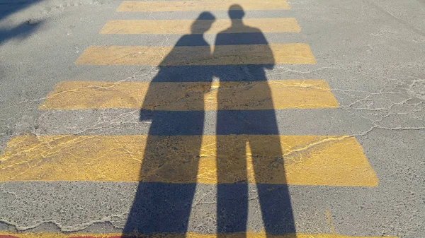 a guy and a girl stand at the beginning of a pedestrian crossing, where it is written stop and wait the passing of time, on the yellow lines drawn on the sidewalk, the shadow is clearly visible