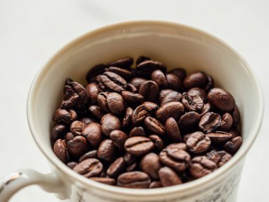 Makro yakın plan kahve çekirdekleri beyaz arka planda beyaz porselen bir fincanda.