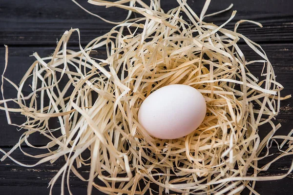 Egg in straw nest on black wooden desk. Top view closeup