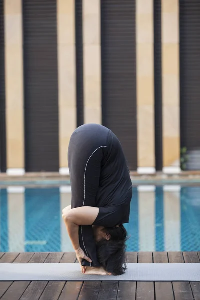 woman practicing yoga, doing head to knees, uttanasana exercise, Standing forward bend pose, working out, wearing sportswear, black pants and top,in nature.