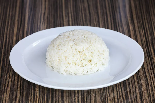 The cooked rice is placed in a white bowl. The backdrop is a wooden board. Steamed rice