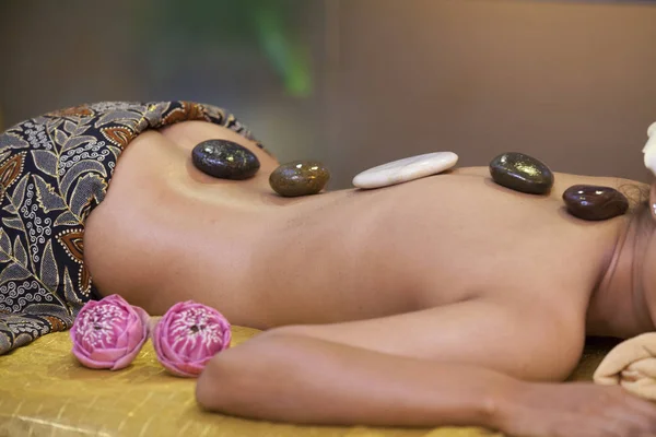 Beautiful woman having hot stones on her back in spa salon. concept of healthcare and female beauty. view of the woman\'s back with hot stones from the front