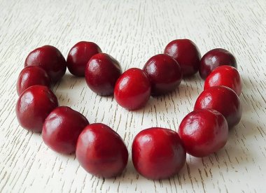 Tatlı kiraz Burgundy taze çilek bir kalp şeklinde hafif bir arka plan üzerinde yalan