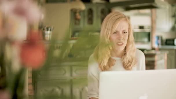 年轻的金发白人妇女坐在家里的一张桌子 看着她的笔记本电脑从一边到一边非常震惊和厌恶 — 图库视频影像