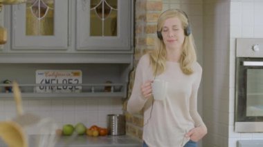Mutlu kadın mutfakta bir kahve bardağı tutan onu kulaklık mutlu kadın mutfakta kulaklık müzik dinlerken müzik dinlerken
