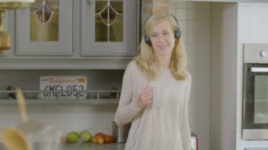 Mutfakta gülümseyen kadın kahve dansı içiyor ve kulaklıkla müzik dinliyor