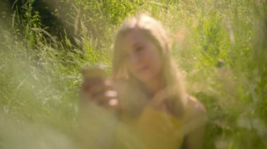 Huzurlu genç sarışın beyaz kadın onu Akıllı Telefon bakarak güzel güneşli açık havada çim rahatlatıcı. 4k Yavaş çekim