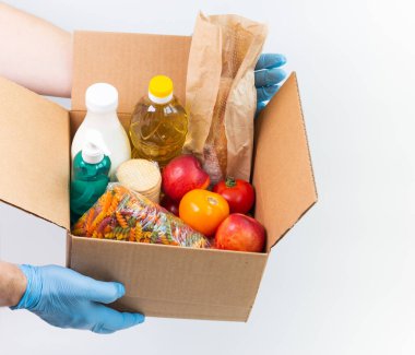 Lateks eldivenli adamın elinde sipariş edilmiş malların olduğu bir kutu var. Güvenli yemek teslimatı karantina altında. Çevrimiçi gıda alışverişi ya da bağış konsepti. Beyaz arka plan. Yüksek kalite yakın çekim fotoğrafı.