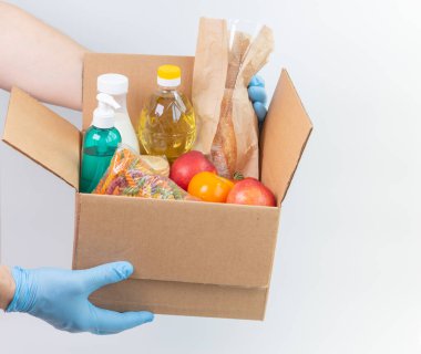 Lateks eldivenli adamın elinde sipariş edilmiş malların olduğu bir kutu var. Güvenli yemek teslimatı karantina altında. Çevrimiçi gıda alışverişi ya da bağış konsepti. Beyaz arka plan. Yüksek kalite yakın çekim fotoğrafı.