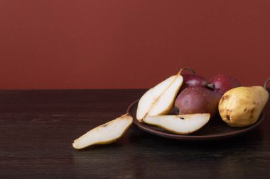 Olgun organik kırmızı ve sarı armutlar ve koyu ahşap zemin üzerinde kil bir kasede armut dilimleri. Taze armut kapanışı. Sarı ve kırmızı armutlu bir arka plan. Yüksek kalite fotoğraf