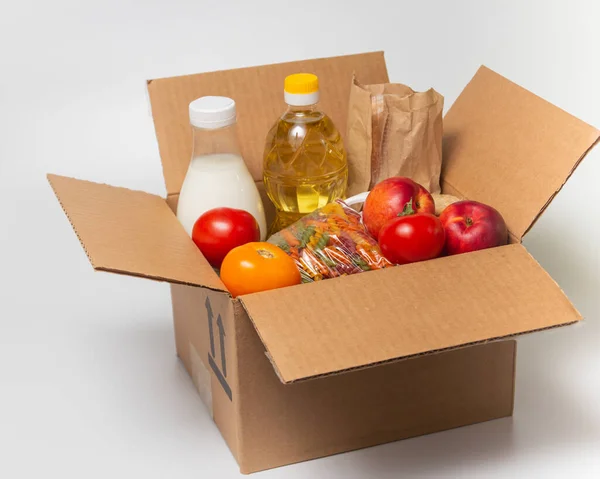 Donation goods in carton box on the white background. Pasta, milk, bread, sunflower oil, tomatoes, peaches. Food delivery for those who need. Quarantine help concept. High quality photo