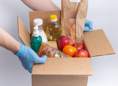 Lateks eldivenli adamın elinde sipariş edilmiş malların olduğu bir kutu var. Güvenli yemek teslimatı karantina altında. Çevrimiçi gıda alışverişi ya da bağış konsepti. Beyaz arka plan. Yüksek kalite yakın çekim fotoğrafı.