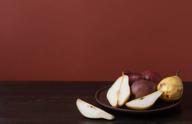 Olgun organik kırmızı ve sarı armutlar ve koyu ahşap zemin üzerinde kil bir kasede armut dilimleri. Taze armut kapanışı. Sarı ve kırmızı armutlu bir arka plan. Yüksek kalite fotoğraf