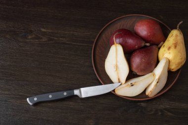 Olgun organik kırmızı ve sarı armutlar ve koyu ahşap zemin üzerinde bıçak bulunan bir kil kasede armut dilimleri. Taze armut kapanışı. Sarı ve kırmızı armutlu arka plan. Yüksek kalite fotoğraf