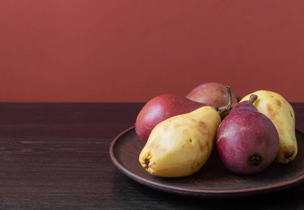 Ripe organic red and yellow pears in a clay bowl on a dark wooden background. Fresh pear closeup. Background with yellow and red pears. High quality photo