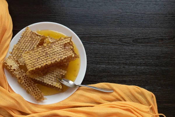 Honeycombs med sked i vit platta på träbordet. Naturlig ekologisk biprodukt. En hälsosam livsstil. Kopiera utrymme för din text. — Stockfoto