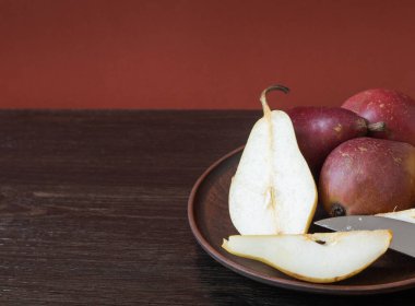 Olgun organik kırmızı ve sarı armutlar ve koyu ahşap zemin üzerinde bıçak bulunan bir kil kasede armut dilimleri. Taze armut kapanışı. Sarı ve kırmızı armutlu arkaplan.