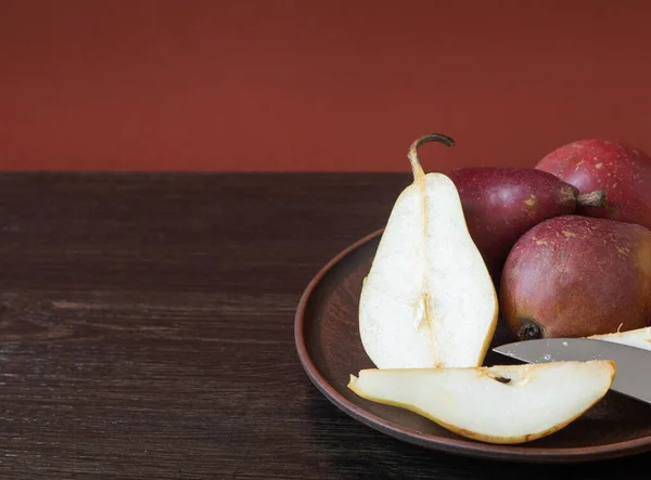 Ripe organic red and yellow pears and slices of pears in a clay bowl with knife on a dark wooden background. Fresh pear closeup. Background with yellow and red pears. — Stock Photo, Image