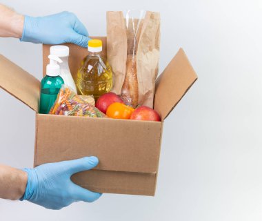 Lateks eldivenli adamın elinde sipariş edilmiş malların olduğu bir kutu var. Güvenli yemek teslimatı karantina altında. Çevrimiçi gıda alışverişi ya da bağış konsepti. Beyaz arka plan. Yüksek kaliteli yakın plan fotoğraf.