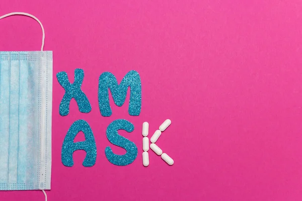 Pembe arka planda tıbbi koruyucu maske. Xmas yazıtları. Noel ve Yeni Yıl kartı, afiş, reklam konsepti. Üstten görüntü, minimalizm, kopyalama alanı. Tıbbî olarak. Yüksek kalite fotoğraf