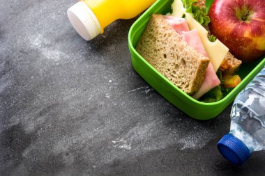 Sağlıklı okul öğle yemeği kutusu: sandviç, sebze, meyve ve siyah taş suyu. Üstten görünüm